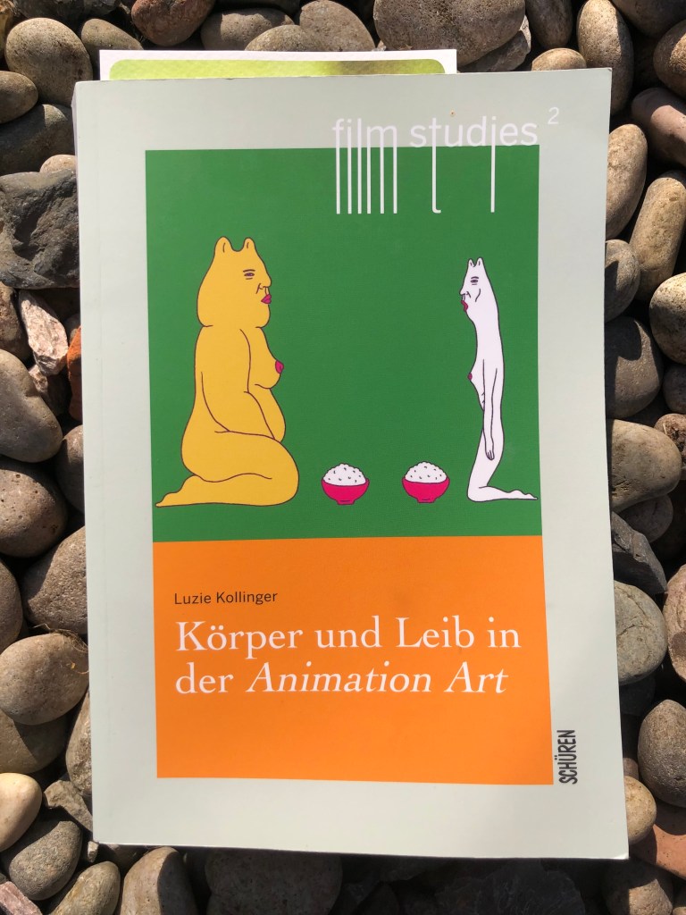 Cover of a paperback book, with an image of two female cat-like characters, drawn kneeling opposite each other on a green background. The title is below on an orange background. The book is pictured on pebbles in the sunshine. 